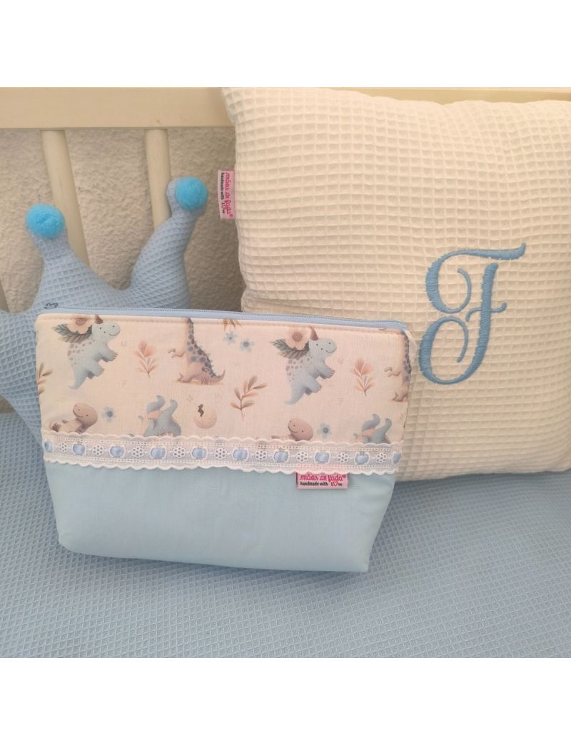 Necessaire azul com padrão de dinossauros em tons de azul e creme. Com bordado inglês e fita de cetim azul