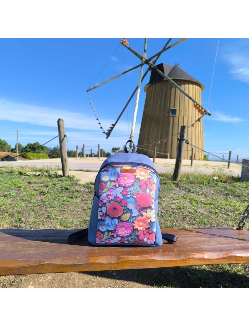 Mochila de senhora artesanal azul com painel frontal em tecido estampado de flores coloridas. Pousada em madeira, com moinho português em fundo