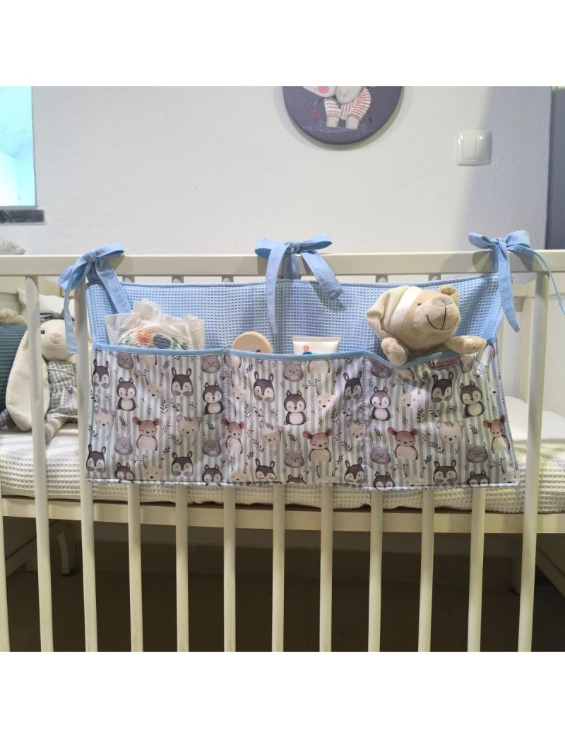 Organizador de cama para bebé com padrão de animais delicados conjugado com waffle azul claro, com três bolsos, pendurado num berço branco e com brinquedos e acessórios de bebé no interior