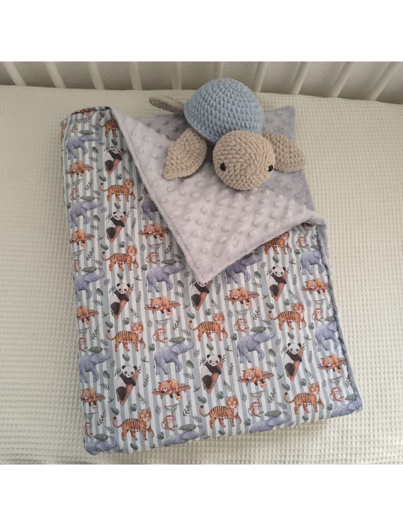 Manta de bebé em tecido com estampado de animais fofos sobre riscas verdes e brancas. O interior é forrado a tecido Minky cinzento. Está dobrada em cima de uma caminha, com uma tartaruga em amigurumi (como decoração)