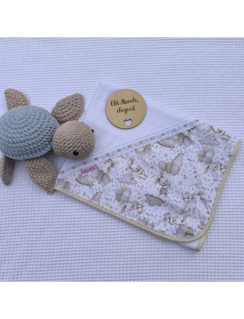 Fralda branca com canto com padrão de coelhos e balões em tons de bege e cinza. Bordado inglês com fita de cetim cinzenta. Tartaruga e placa decorativa cm a descrição "Mãos de Fada "
