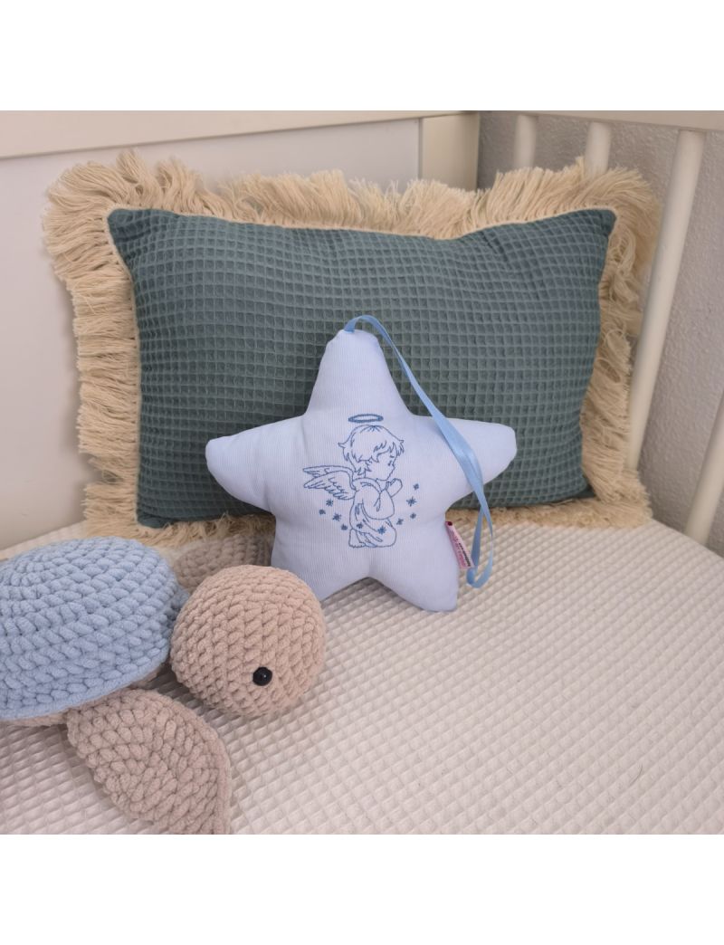 Estrela azul claro com anjo bordado, fita azul claro e enchimento antialérgico, apoiada em almofadas decorativas num quarto de bebé.