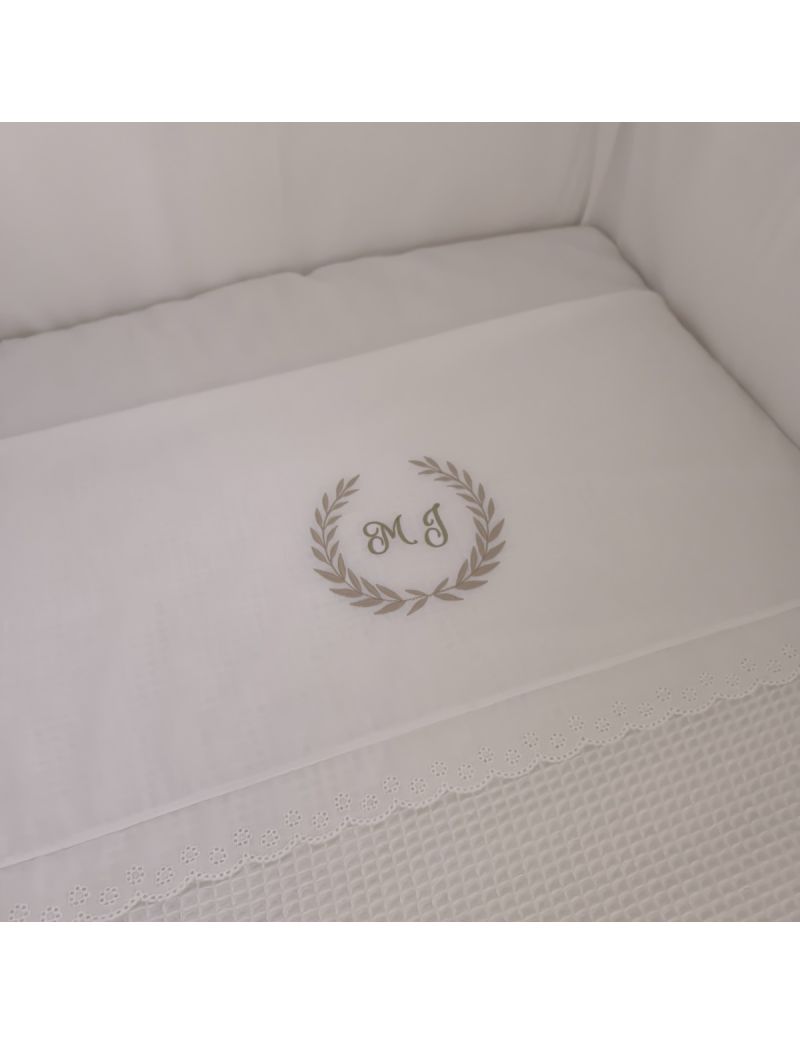 Lençol de bebé com monograma com as letras MJ, com barra em bordado inglês, colocados numa cama de grades 