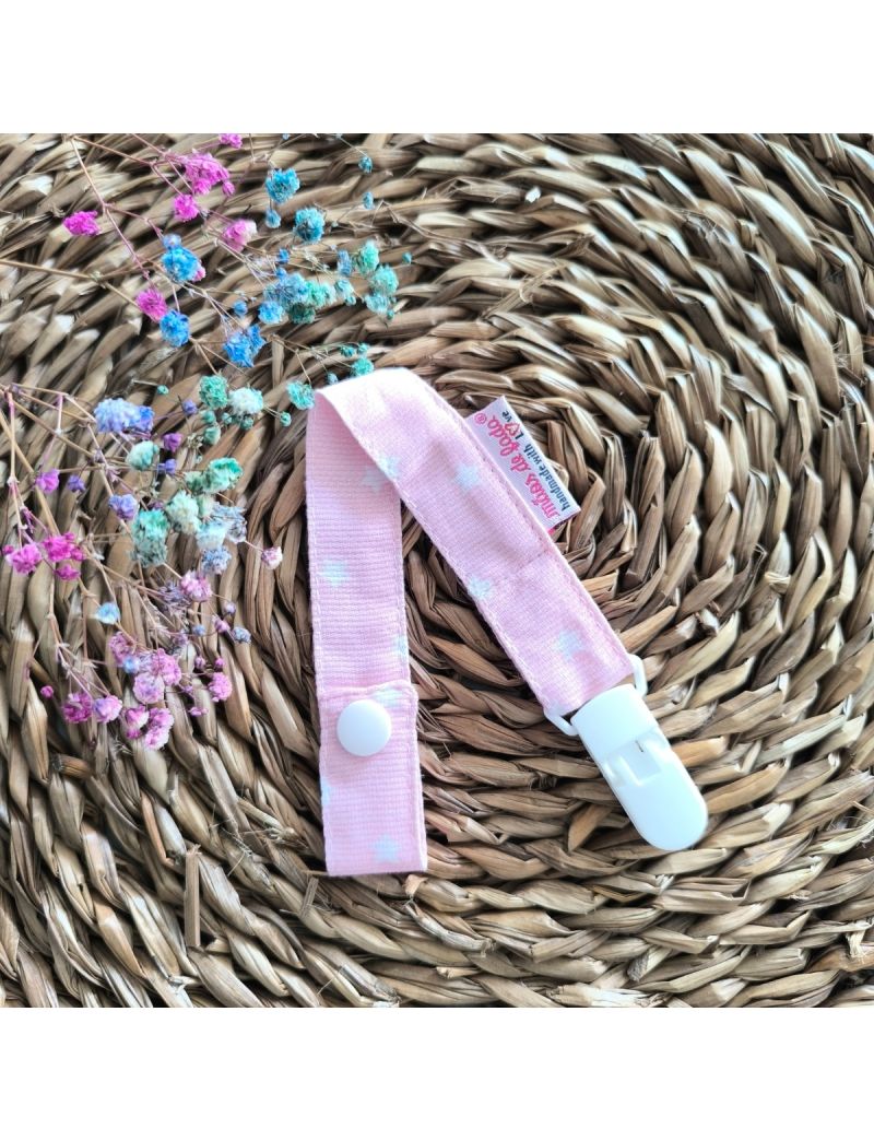 Fita de chucha em tecido de algodão rosa com estrelas brancas, com mola de plástico branca, colocada sobre base de palha artesanal. 