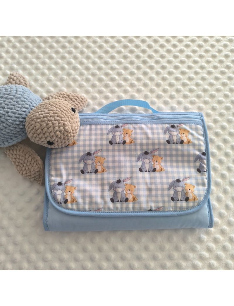 Bolsa multiusos para beb&eacute; fechada com padr&atilde;o de xadrez vichy azul e branco. O tecido destaca ilustra&ccedil;&otilde;es das personagens Winnie the Pooh e o burro Eeyore abra&ccedil;ados, rodeados por pequenas abelhas e flores. A bolsa tem um acabamento com vivo em azul claro, 
