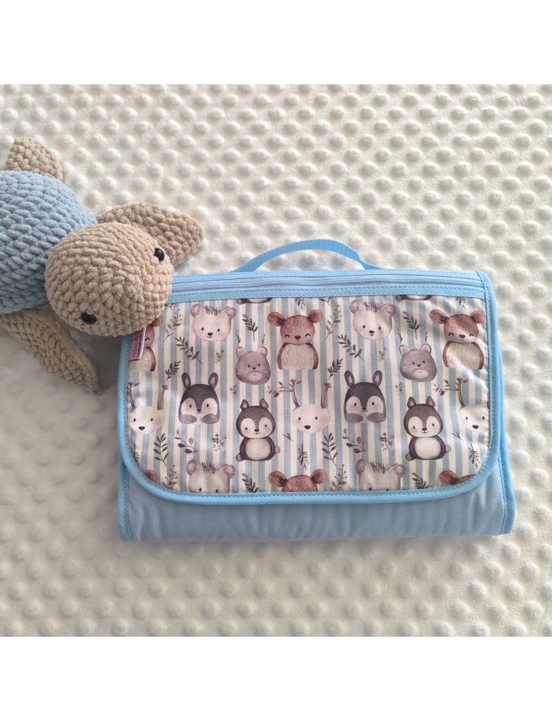 Bolsa multiusos com padr&atilde;o de animais da floresta (esquilos, guaxinins e veados) em tons de castanho e azul. A bolsa est&aacute; fechada e possui uma bolsa no exterior com fecho ziper azul claro. Al&ccedil;a azul claro