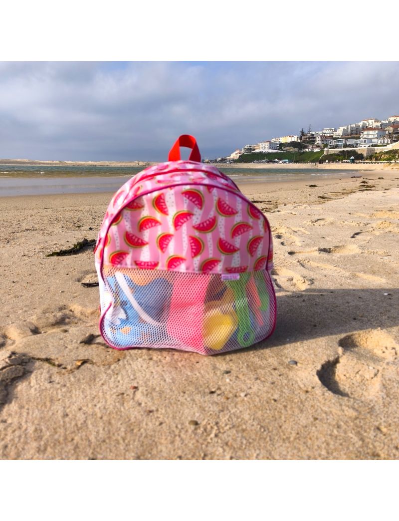 Mochila infantil de praia com padr&atilde;o vibrante de fatias de melancia sobre fundo rosa e branco &agrave;s riscas. A parte inferior &eacute; feita de rede branca, revelando brinquedos de praia no interior