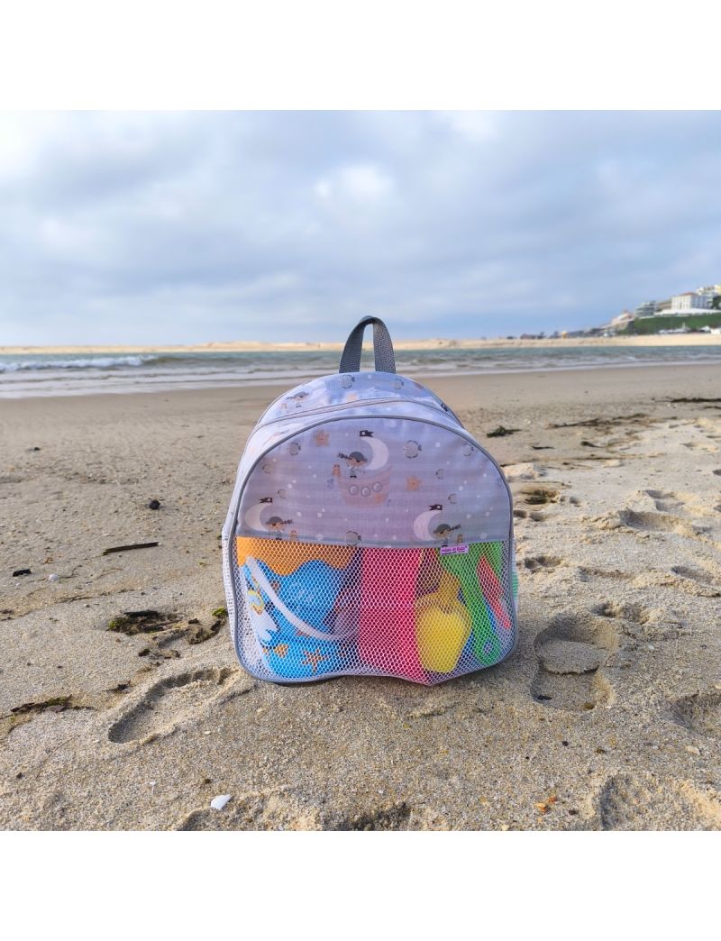 Mochila infantil de praia em tons de cinza claro com padr&atilde;o de piratas navegando em barcos em formato de lua crescente. A mochila possui uma base de rede branca com brinquedos coloridos vis&iacute;veis no interior