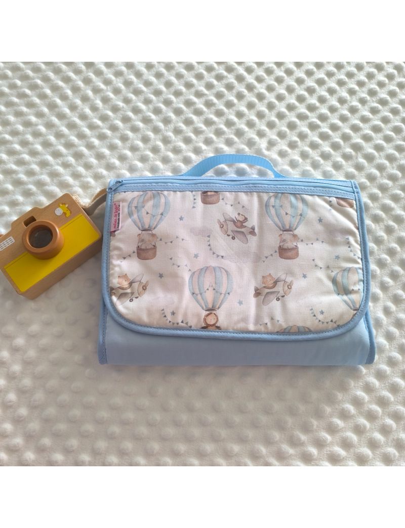 Bolsa multiusos fechada com uma bolsa frontal. Padr&atilde;o de bal&otilde;es de ar quente em tons de azul e avi&otilde;es em tons de cinza e creme . Fecho z&iacute;per azul