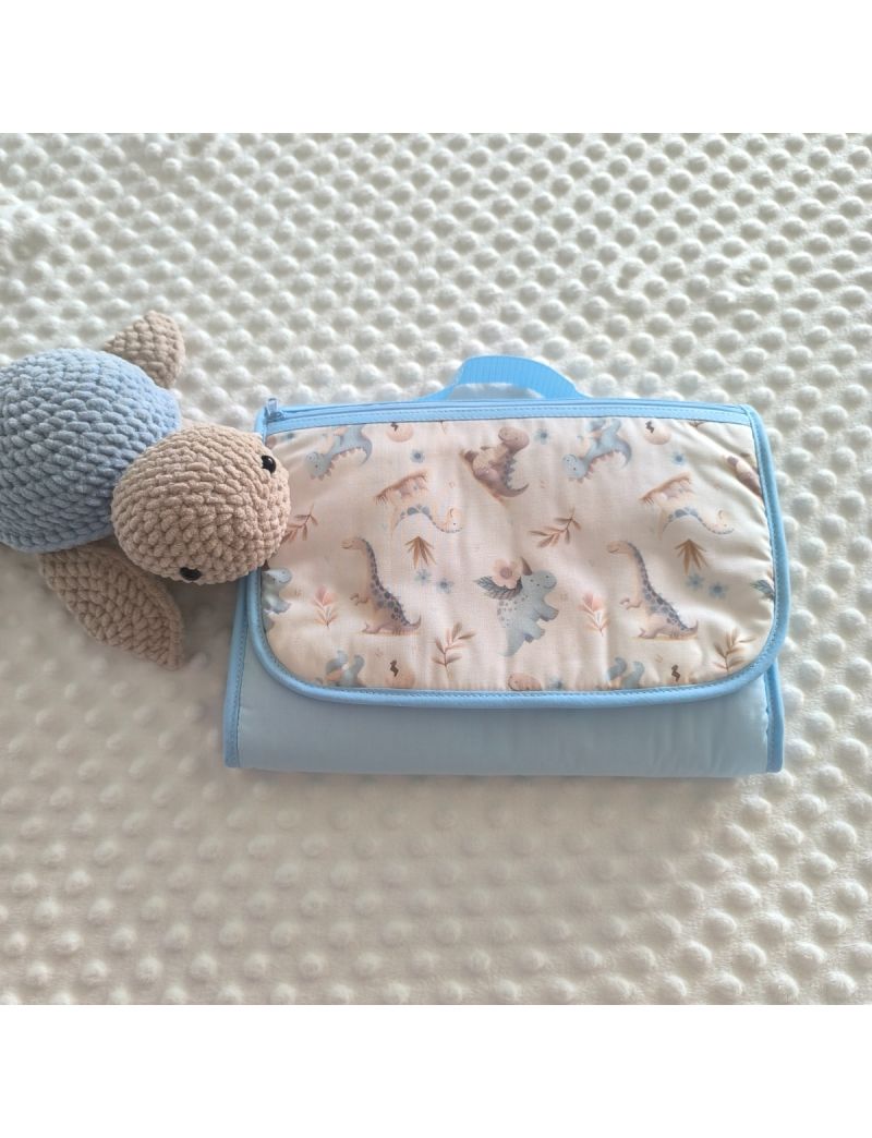 Bolsa multiusos fechada com uma bolsa frontal. Padr&atilde;o dinossauros em tons de azul e creme conjugado com um tecido azul liso. Fecho z&iacute;per e al&ccedil;a de m&atilde;o azul