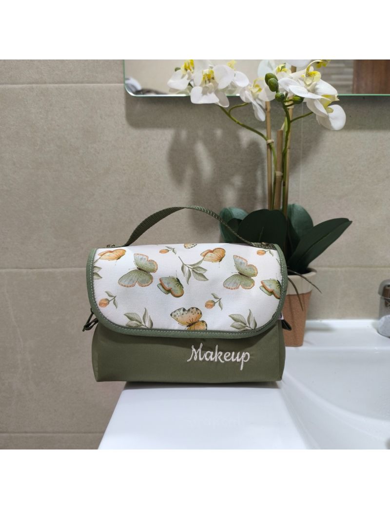 Bolsa de maquilhagem compacta com padr&atilde;o de borboletas em tons de verde, colocada sobre uma bancada de casa de banho.