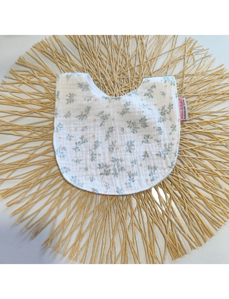 Babete de mola infantil feito em musselina org&acirc;nica texturizada branca, com um padr&atilde;o delicado de ramos verde seco e flores pequeninas em tons p&ecirc;ssego.