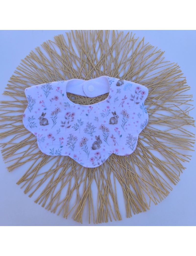 : Babete infantil com design em formato de flor ou gola com bordas onduladas que imitam p&eacute;talas. &Eacute; feito em musselina de algod&atilde;o branca com o padr&atilde;o Bosque M&aacute;gico, composto por ilustra&ccedil;&otilde;es delicadas de pequenos coelhos sentados e raminhos de flores silves