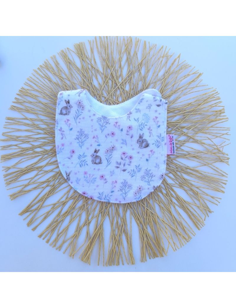 Babete de mola infantil de formato arredondado, feito em musselina org&acirc;nica branca com um padr&atilde;o ilustrado e delicado de pequenos coelhos sentados e raminhos de flores silvestres em tons suaves de rosa, lil&aacute;s e azul-acinzentado