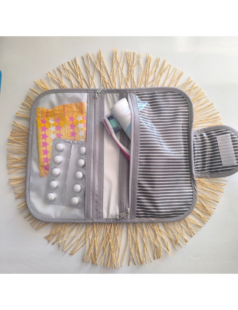 Bolsa de higiene plastificada com padr&atilde;o de riscas azuis cinza e brancas, aberta, com compartimentos para higiene oral, medica&ccedil;&atilde;o e produtos femininos.
