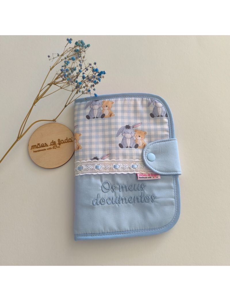 Porta documentos em formato livro com padrão azul liso conjugado com padrão do burro e do urso (Winnie The Pooh), com bordado inglês com fita cetim azul, com a inscrição “Os meus documentos” bordado a azul