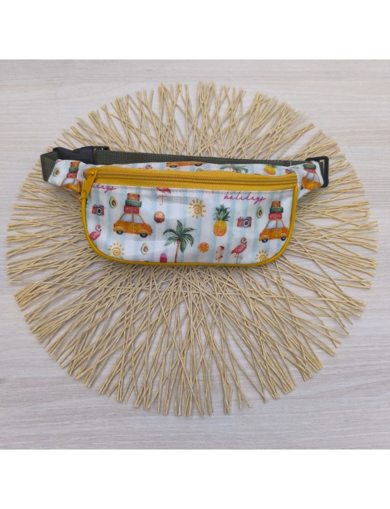 Bolsa de cintura com carrinhos de viagem com malas no topo. Padrão com ananáses, flamingos, máquina fotográfica, sol, etc. Fecho amarelo e alça verde seco 