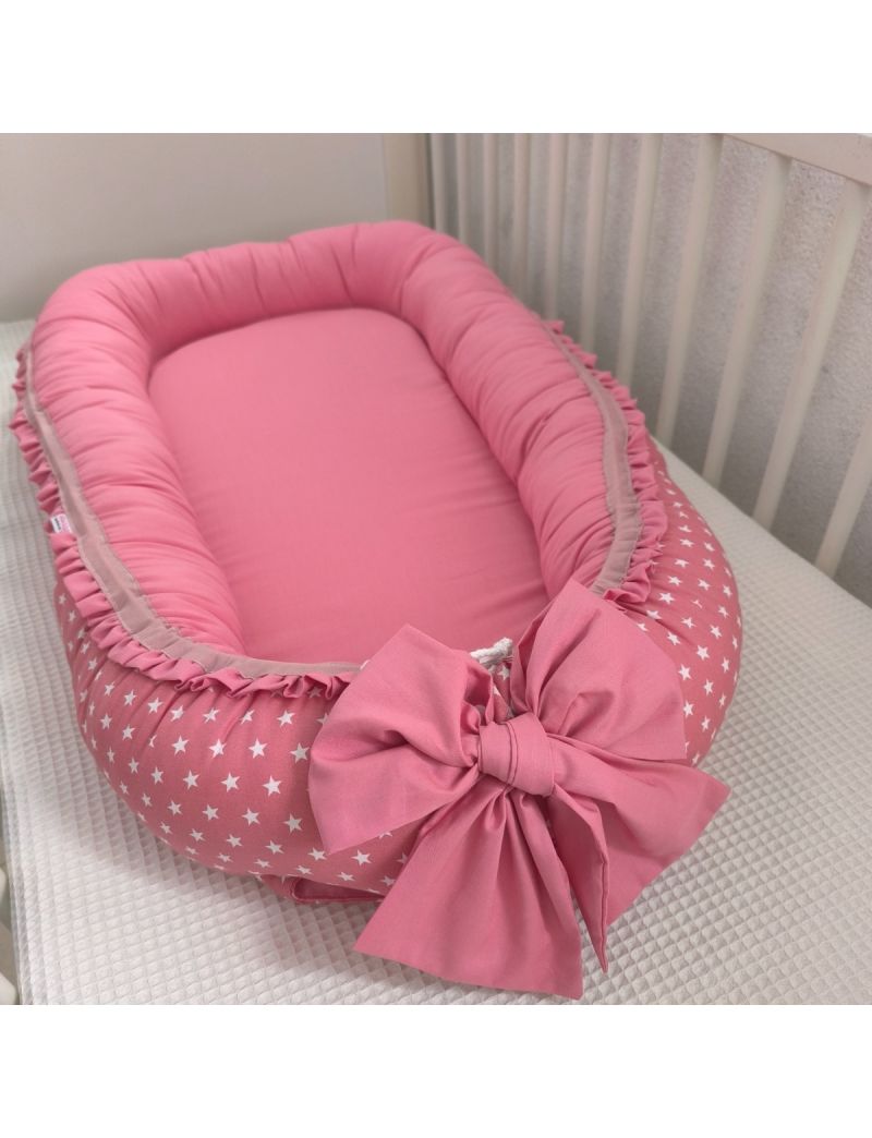 Ninho de bebé em rosa velho no exterior com estrelas brancas e rosa velho liso no interior. Folho de contorno do ninho e laço à frente em rosa velho. Ninho colocado na cama de grades 