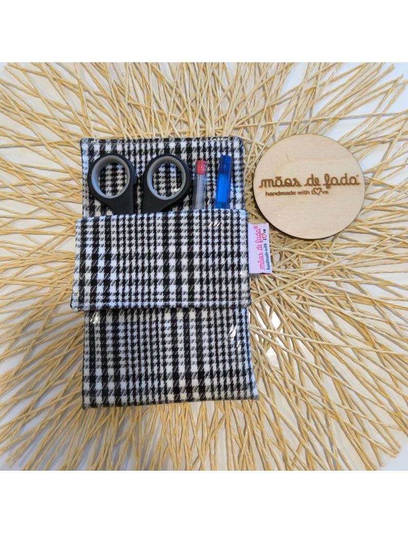 Bolsa para bata plastificada com padrão preto e branco, contendo canetas e tesoura, ao lado de um logótipo em madeira com a designação “mãos de fada handmade with love"
