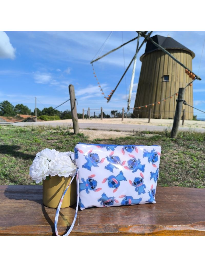 Necessaire em tecido plastificado com padrão do Stitch, colocada sobre banco de madeira com flores brancas decorativas e moinho ao fundo, em ambiente ensolarado e descontraído