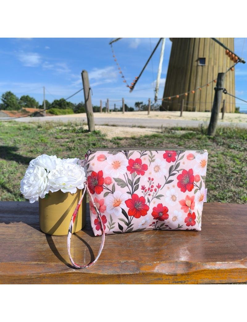 Necessaire em tecido plastificado bege com padrão floral vermelho, pousada sobre uma superfície de madeira, destacando o seu design elegante e feminino