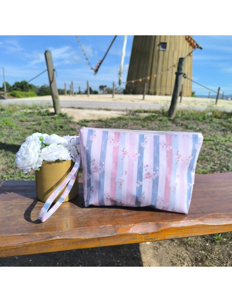 Necessaire em tecido plastificado com padrão floral delicado, pousada sobre uma superfície de madeira, em ambiente luminoso que realça o seu estilo feminino e elegante