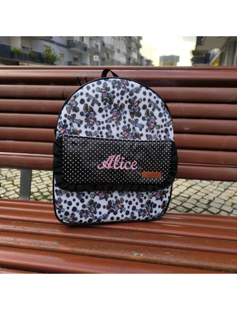 Mochila de criança com padrão da Minnie em tons de preto. Pala da mochila preta com bolinhas brancas e o nome Alice bordado a cor de rosa claro. Folho preto