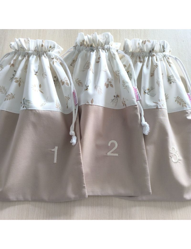 Tr&ecirc;s taleigos organizadores de beb&eacute; alinhados, em tons de bege e branco. A parte superior tem um padr&atilde;o de pequenas avionetas e folhas em tons terra, enquanto a parte inferior bege exibe os n&uacute;meros 1, 2 e 3 bordados em linha clara. Os sacos t&ecirc;m fecho de c