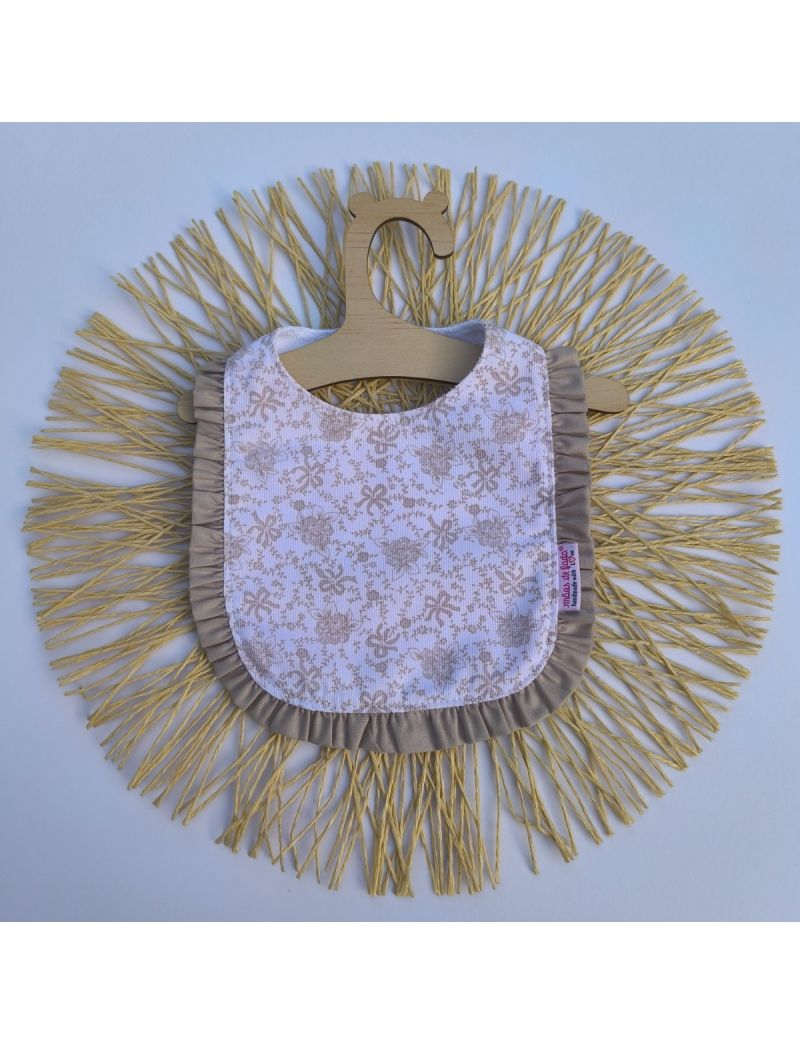 Babete branco com padrão floral bege. Folho bege a contornar o babete 