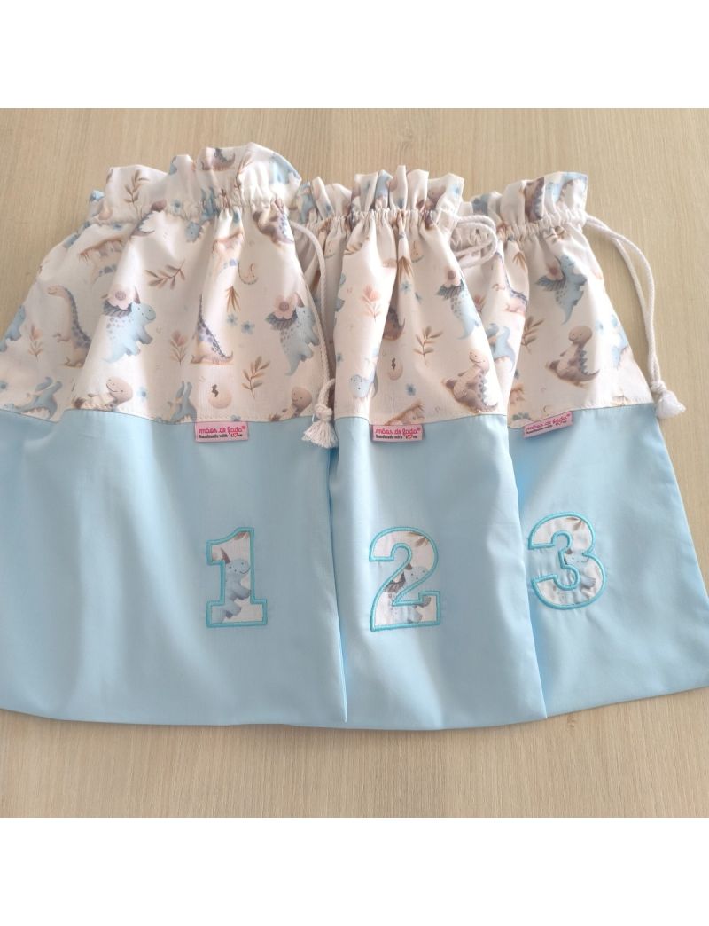 Conjunto de 3 taleigos para maternidade, com base azul claro e topo com padrão de dinossauros.Numerados com  "1, 2 e 3". 