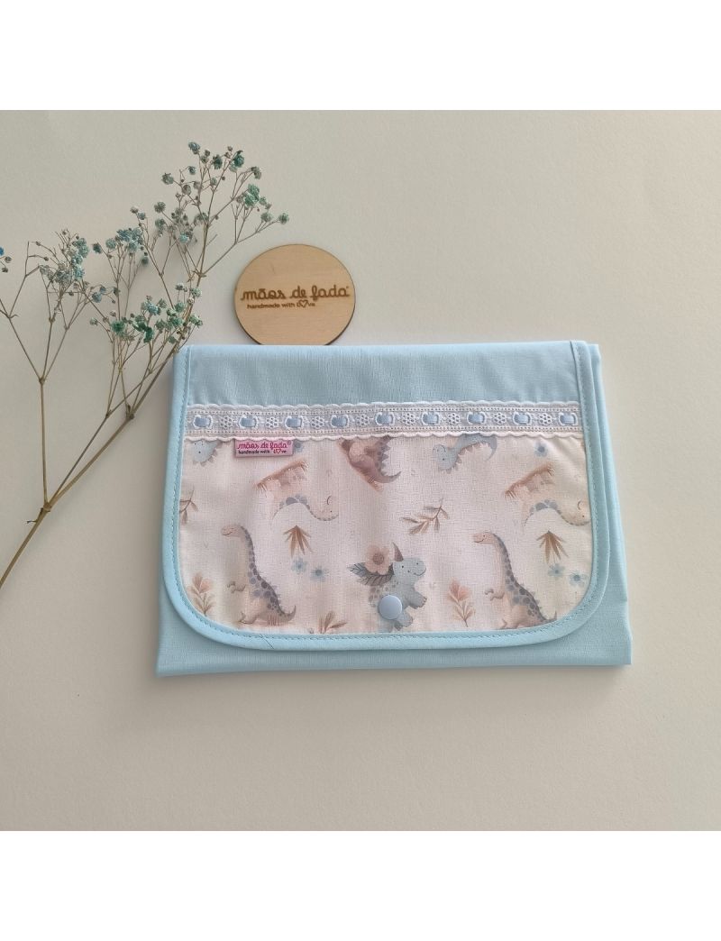 Muda fralda fechado com tecido azul conjugado com um padrão de dinoussauros em tons suaves. Com bordado inglês com fita azul