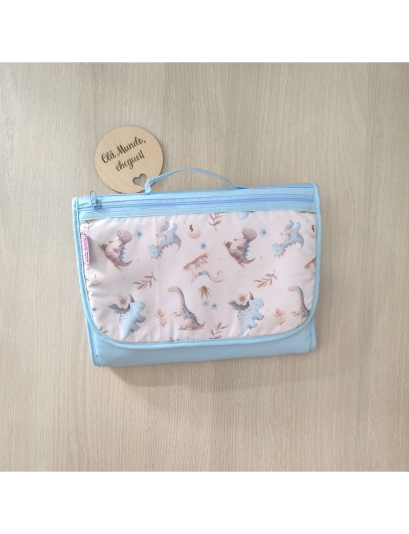 Bolsa multiusos fechada com uma bolsa frontal. Padrão dinossauros em tons de azul e creme conjugado com um teciso azul liso. Fecho zíper e alça de mão azul