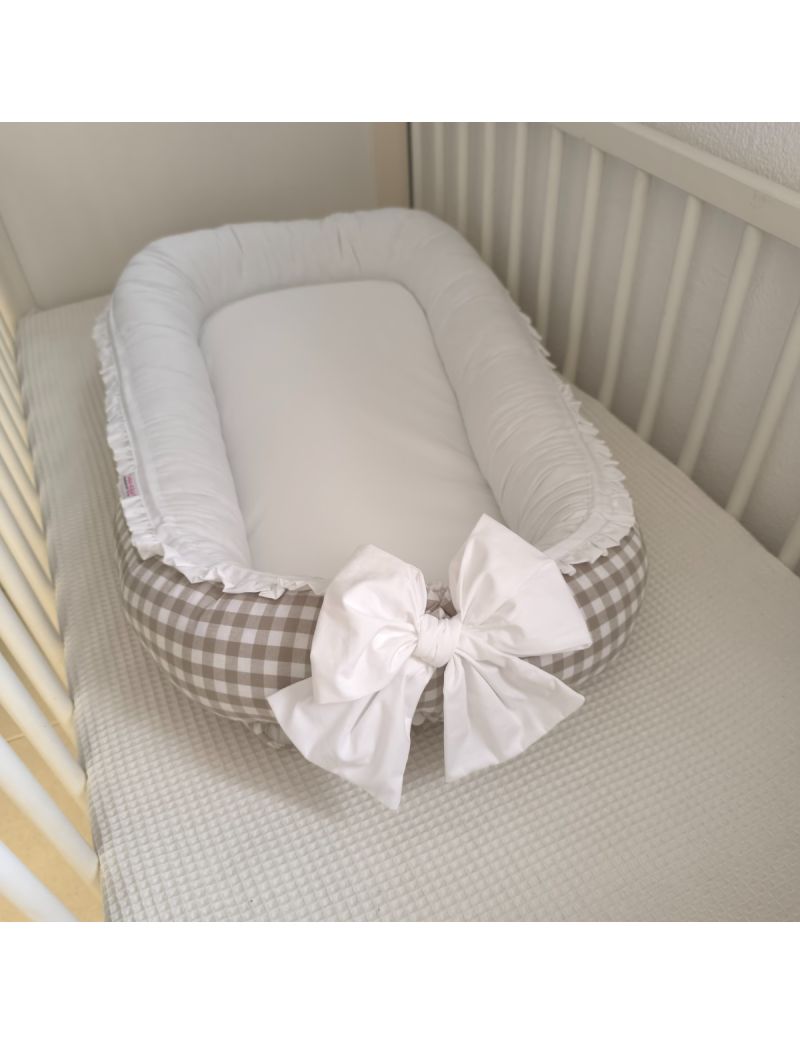 Ninho redutor de berço versátil para bebé, em tecido algodão respirável com padrão Vicky bege. Laço frontal e folhinho branco a contornar o ninho. Ninho colocado dentro do berço branco  