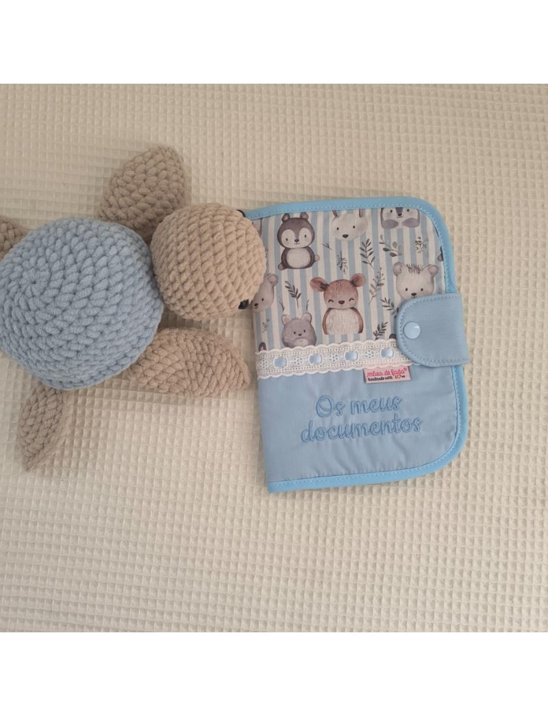 Porta documentos em formato livro  com padrão de animais delicados na parte de cima e azul liso com a descrição "Os meus documentos" em azul na parte de baixo. Bordado inglês na junção dos dois tecidos. Tartaruga em amigurumi a decorar 