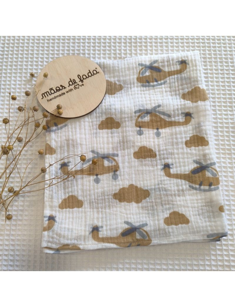 ralda Musselina branca com padrão de helicópteros e nuvens em tons de camel. Placa de madeira com a inscrição "mãos de fada" e um ramos a decorar 