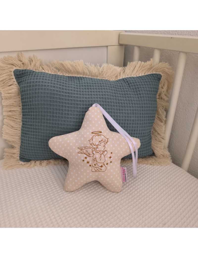 Estrela bege com anjo bordado a castanho, fita branca e enchimento antialérgico, apoiada em almofadas decorativas num quarto de bebé