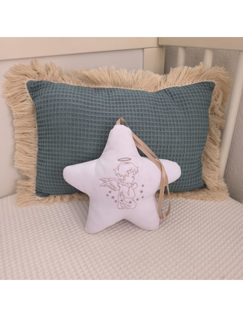 Estrela com um Anjo bordado a bege colocada numa caminha de bebé. Atrás tem uma almofada decorativa verde 