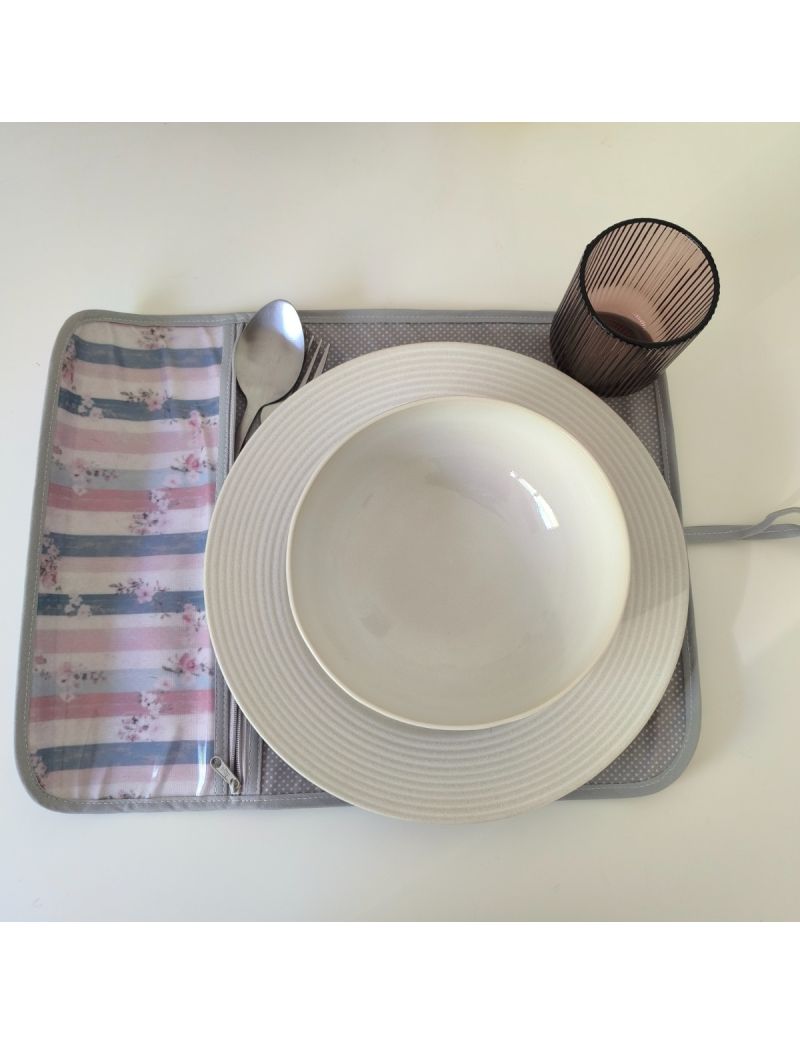 Individual aberto com padrão de flores delicadas sobre riscas azuis e rosa na parte da bolsa para os talheres. Restante individual cinza com bolinhas brancas.