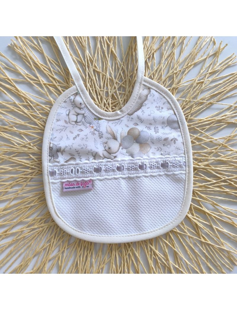 Babete de atar com padrão de coelhinhos e balões em tons de bege e cinza conjugado com tecido branco. Bordado inglês com fita de cetim cinzenta 