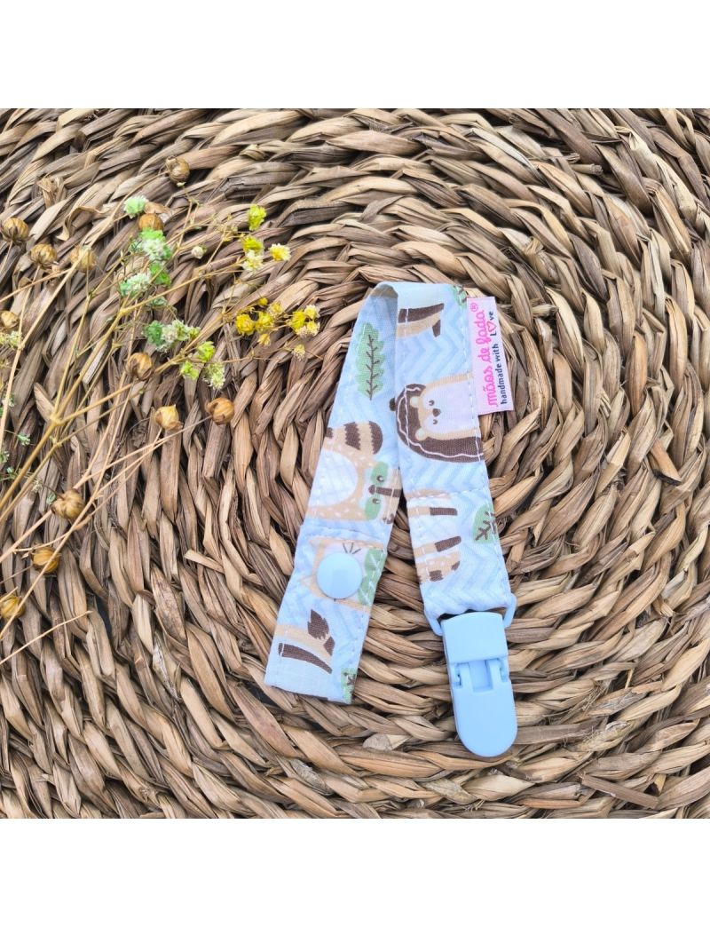 Fita de chucha em tecido cheveron azul com animais, com mola de plástico azul, colocada sobre base de palha artesanal. 