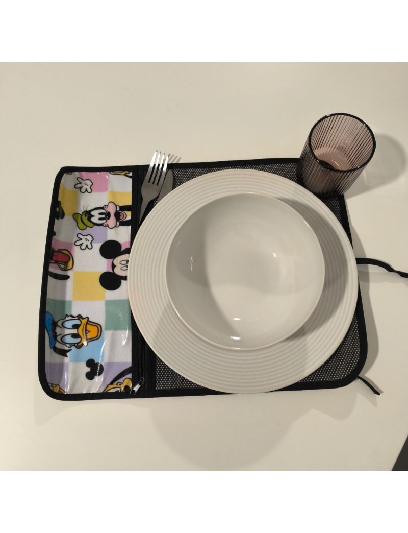 Individual aberto. Bolso para os talheres com tecido da Disney (Pateta, Mickey, Pato Donald) e restante individual preto com bolinhas brancas. Prato, talheres e copo colocado no individual