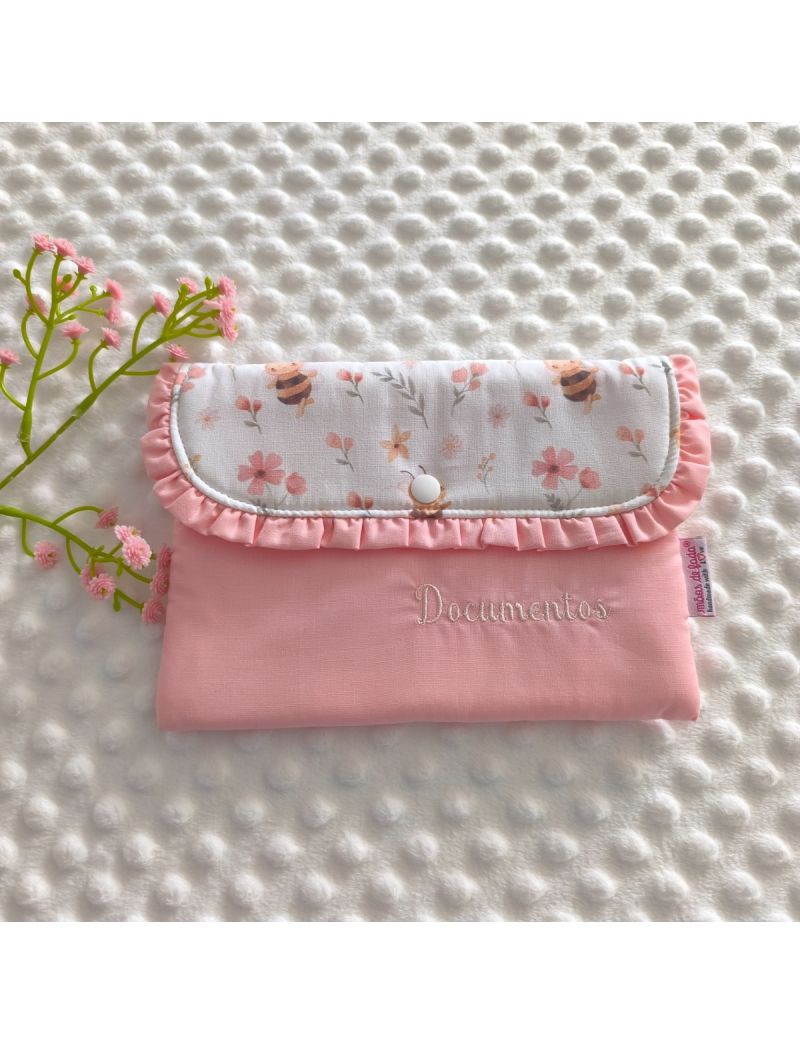 Porta-documentos em formato envelope para beb&eacute;. A parte superior tem um padr&atilde;o de abelhinhas e flores pequenas, enquanto a parte inferior s&atilde;o em tecido rosa liso. Possui um folho na pala em rosa