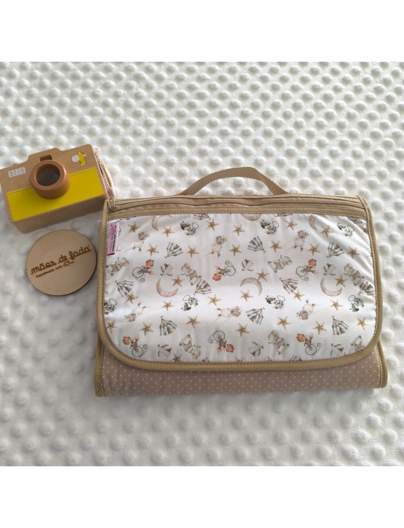 Bolsa multiusos para beb&eacute; fechada, com al&ccedil;a de m&atilde;o superior. O padr&atilde;o exterior destaca o tema circo com animais em bicicletas, tendas, estrelas e luas crescentes sobre fundo branco, complementado por um tecido inferior em bege com pequenas bolinhas branca