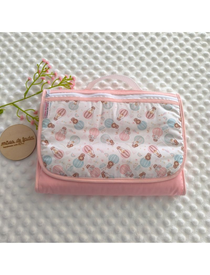 Bolsa multiusos para beb&eacute; fechada e compacta. Destaca-se o padr&atilde;o exterior com ilustra&ccedil;&otilde;es de bal&otilde;es de ar quente em tons pastel de rosa e turquesa sobre fundo branco, com acabamentos e rebordo em rosa suave. Possui um fecho superior e uma al&ccedil;a de m&atilde;o