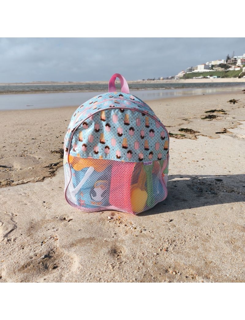 Mochila infantil de praia com padr&atilde;o de gelados e picol&eacute;s coloridos sobre fundo azul claro, com acabamentos em rosa. A parte inferior &eacute; feita de rede branca, revelando brinquedos de praia coloridos no interior