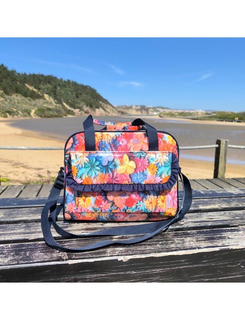 Lancheira t&eacute;rmica com padr&atilde;o tropical de  flores e borboletas 3D em v&aacute;rias cores. Destaca-se a bolsa frontal com pala e folho azul escuro, as al&ccedil;as de m&atilde;o e a al&ccedil;a a tiracolo regul&aacute;vel tamb&eacute;m em azul escuro