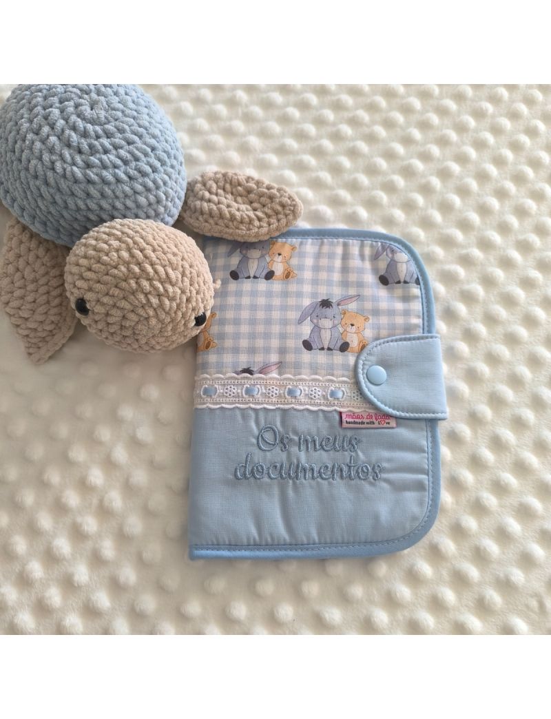 Porta documentos em formato livro com padr&atilde;o azul liso conjugado com padr&atilde;o do burro e do urso (Winnie The Pooh), com bordado ingl&ecirc;s com fita cetim azul, com a inscri&ccedil;&atilde;o &ldquo;Os meus documentos&rdquo; bordado a azul