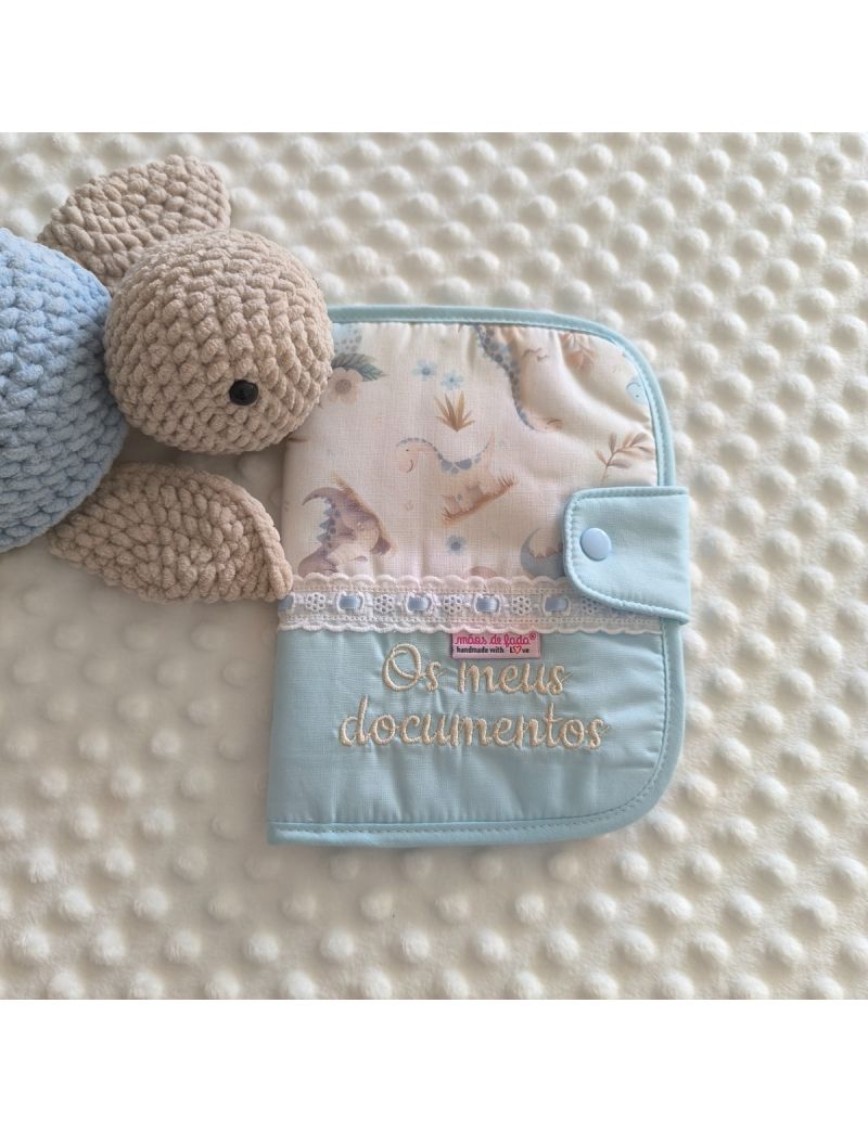 Porta documentos em formato livro com tecido azul conjugado com um padr&atilde;o de dinossauros em tons suaves. Possui bordado ingl&ecirc;s com fita de cetim azul e a inscri&ccedil;&atilde;o "Os meus documentos"