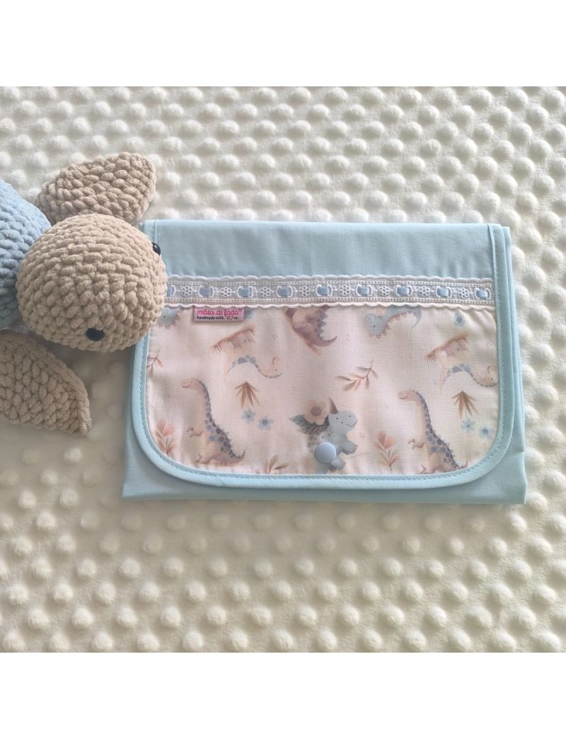 Muda fralda fechado com tecido azul conjugado com um padr&atilde;o de dinossauros em tons suaves. Com bordado ingl&ecirc;s com fita azul