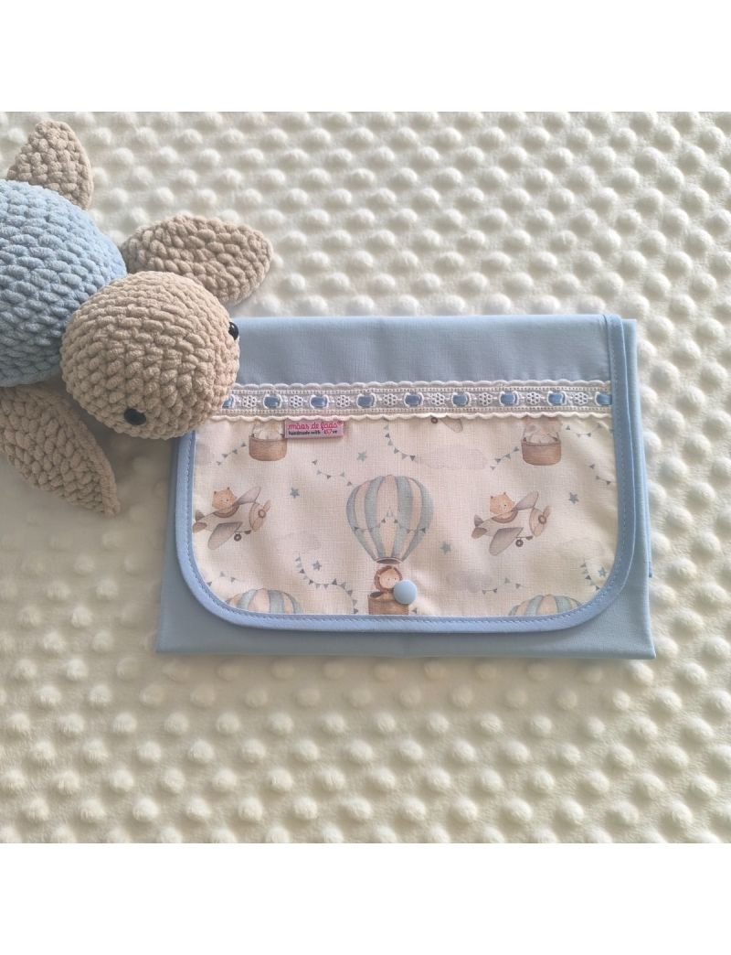 Muda fralda fechado com tecido azul conjugado com um padr&atilde;o de bal&otilde;es de ar quente e avi&otilde;es  em tons suaves. Com bordado ingl&ecirc;s com fita azul 